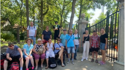 Fröhliche Menschen sitzen in Sommerkleidung auf einer Mauer und stehen vor einem Tor im Holiday Park.